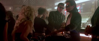 Movie still from “Revenge” (1990), directed by Tony Scott – A group of people standing in a room; Medium shot, Over the shoulder angle