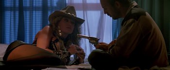 Movie still from “Revenge” (1990), directed by Tony Scott – A woman wearing a cowboy hat and holding a gun; Medium shot, Over the shoulder angle