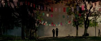 Movie still from “Revenge” (1990), directed by Tony Scott – Two women standing in front of a wall covered in paper flags; Extreme Wide shot, Low angle