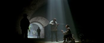Movie still from “Revenge” (1990), directed by Tony Scott – A man holding a sword and a woman sitting on a chair; Wide shot, Low angle