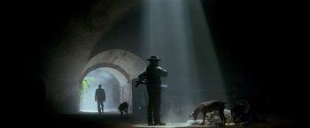 Movie still from “Revenge” (1990), directed by Tony Scott – A man in a hat and a dog in a tunnel; Wide shot, Low angle