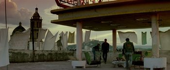 Movie still from “Revenge” (1990), directed by Tony Scott – Two men standing under an awning on the beach; Wide shot, Low angle
