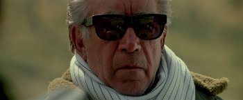 Movie still from “Revenge” (1990), directed by Tony Scott – An older man wearing sunglasses and a scarf; Close Up shot, Low angle