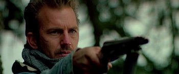 Movie still from “Revenge” (1990), directed by Tony Scott – A person holding a gun; Close Up shot, Low angle