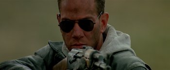 Movie still from “Revenge” (1990), directed by Tony Scott – A person wearing sunglasses and holding a gun; Close Up shot, Low angle