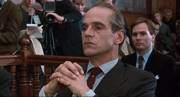 Movie still from “Reversal of Fortune” (1990), directed by Barbet Schroeder – A man in a suit and tie clasps his hands; Close Up shot, Low angle