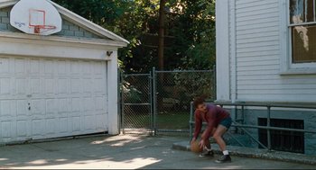 Movie still from “Reversal of Fortune” (1990), directed by Barbet Schroeder – A person standing on the side of a road holding a basketball; Wide shot, High angle