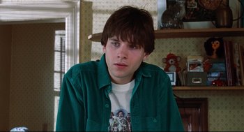 Movie still from “Reversal of Fortune” (1990), directed by Barbet Schroeder – A young man in a green shirt is looking at the camera; Close Up shot, Over the shoulder angle