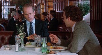 Movie still from “Reversal of Fortune” (1990), directed by Barbet Schroeder – Two men sitting at a table with plates of food in front of them; Medium shot, Over the shoulder angle