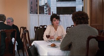 Movie still from “Reversal of Fortune” (1990), directed by Barbet Schroeder – A woman sitting at a table with a glass of wine; Medium shot, Over the shoulder angle