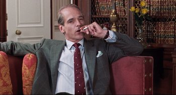 Movie still from “Reversal of Fortune” (1990), directed by Barbet Schroeder – An older man in a suit and tie smoking a cigarette; Medium shot, Low angle