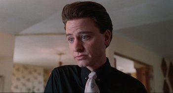 Movie still from “Reversal of Fortune” (1990), directed by Barbet Schroeder – A man in a black dress shirt and tie; Close Up shot, Low angle