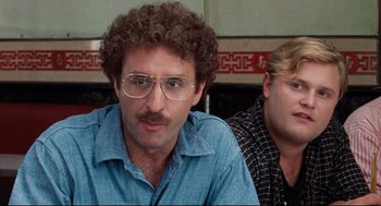 Movie still from “Reversal of Fortune” (1990), directed by Barbet Schroeder – A man with curly hair and glasses sitting next to another man with blonde hair; Close Up shot, Over the shoulder angle