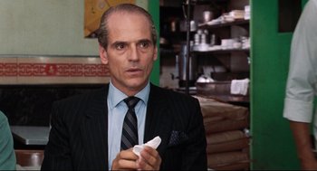 Movie still from “Reversal of Fortune” (1990), directed by Barbet Schroeder – A man wearing a suit and tie holding a paper; Close Up shot, Over the shoulder angle