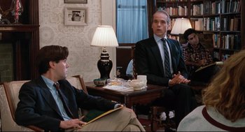 Movie still from “Reversal of Fortune” (1990), directed by Barbet Schroeder – Two men in suits sitting at a table talking to each other; Medium shot, Over the shoulder angle