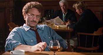 Movie still from “Reversal of Fortune” (1990), directed by Barbet Schroeder – A man sitting at a table in front of a glass of wine; Medium shot, Over the shoulder angle