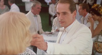 Movie still from “Reversal of Fortune” (1990), directed by Barbet Schroeder – A man in a white suit is holding a woman's hand; Close Up shot, Over the shoulder angle