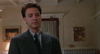 Movie still from “Reversal of Fortune” (1990), directed by Barbet Schroeder – A man wearing a suit and tie standing in front of a wall; Close Up shot, Low angle