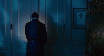 Movie still from “Reversal of Fortune” (1990), directed by Barbet Schroeder – A man standing in front of a door in a room; Medium shot, Over the shoulder angle