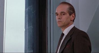 Movie still from “Reversal of Fortune” (1990), directed by Barbet Schroeder – A man wearing a suit and tie standing in front of a window; Close Up shot, Low angle