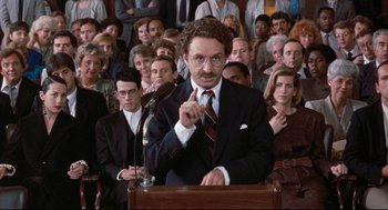 Movie still from “Reversal of Fortune” (1990), directed by Barbet Schroeder – A man giving a speech in front of a crowd; Medium shot, High angle