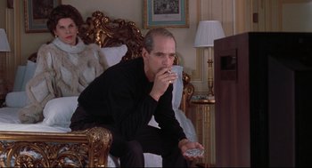 Movie still from “Reversal of Fortune” (1990), directed by Barbet Schroeder – A man sitting on a chair holding a remote control; Medium shot, Over the shoulder angle