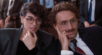 Movie still from “Reversal of Fortune” (1990), directed by Barbet Schroeder – A man and a woman sitting next to each other in front of a crowd; Close Up shot, Over the shoulder angle
