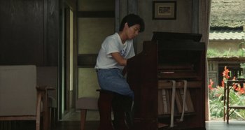 Movie still from “Rhapsody in August” (1991), directed by Akira Kurosawa – A man sitting on a chair playing a piano; Medium shot, Low angle
