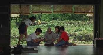 Movie still from “Rhapsody in August” (1991), directed by Akira Kurosawa – A group of people sitting on the ground looking at a tablet computer; Wide shot, High angle