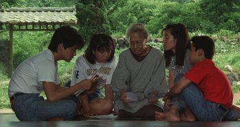 Movie still from “Rhapsody in August” (1991), directed by Akira Kurosawa – An old man sitting on the ground surrounded by young people; Medium shot, High angle