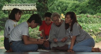 Movie still from “Rhapsody in August” (1991), directed by Akira Kurosawa – An older woman sitting on the ground next to two young boys; Medium shot, High angle