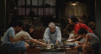Movie still from “Rhapsody in August” (1991), directed by Akira Kurosawa – An old man sitting at a table with a group of people around him; Wide shot, High angle