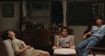 Movie still from “Rhapsody in August” (1991), directed by Akira Kurosawa – A boy sitting in a chair in front of a woman; Wide shot, High angle