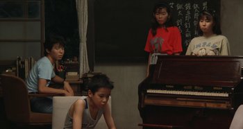 Movie still from “Rhapsody in August” (1991), directed by Akira Kurosawa – A group of young people sitting around a piano; Medium shot, High angle