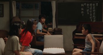 Movie still from “Rhapsody in August” (1991), directed by Akira Kurosawa – A couple of people sitting in front of an open box; Wide shot, Over the shoulder angle