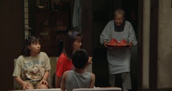 Movie still from “Rhapsody in August” (1991), directed by Akira Kurosawa – A group of people sitting around a table; Medium shot, Over the shoulder angle