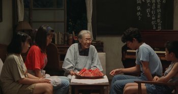 Movie still from “Rhapsody in August” (1991), directed by Akira Kurosawa – An old man sitting at a table with a tray of watermelon; Wide shot, High angle