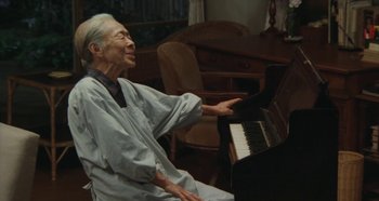 Movie still from “Rhapsody in August” (1991), directed by Akira Kurosawa – An older man sitting in front of a piano; Medium shot, High angle