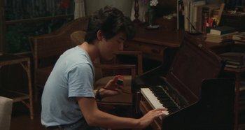 Movie still from “Rhapsody in August” (1991), directed by Akira Kurosawa – A young man playing the piano in a living room; Medium shot, High angle