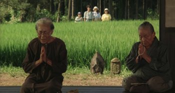 Movie still from “Rhapsody in August” (1991), directed by Akira Kurosawa – An old man praying in front of a group of people in a field; Wide shot, Low angle