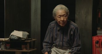 Movie still from “Rhapsody in August” (1991), directed by Akira Kurosawa – An older woman sitting in a chair in front of a wall; Medium shot, High angle