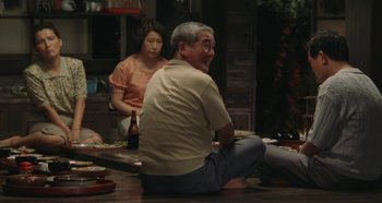 Movie still from “Rhapsody in August” (1991), directed by Akira Kurosawa – An older man sitting on the ground with a bottle of beer; Wide shot, Over the shoulder angle