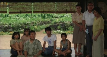 Movie still from “Rhapsody in August” (1991), directed by Akira Kurosawa – A group of people sitting on the ground in front of a building; Wide shot, High angle
