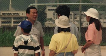 Movie still from “Rhapsody in August” (1991), directed by Akira Kurosawa – A group of people standing next to each other on a field; Medium shot, Over the shoulder angle