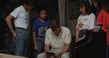 Movie still from “Rhapsody in August” (1991), directed by Akira Kurosawa – A group of young people standing around a man holding a tablet; Medium shot, High angle
