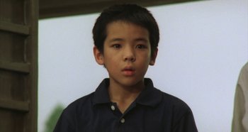 Movie still from “Rhapsody in August” (1991), directed by Akira Kurosawa – A boy in a blue shirt is looking at the camera; Close Up shot, High angle
