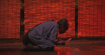 Movie still from “Rhapsody in August” (1991), directed by Akira Kurosawa – A man sitting on the ground looking at a cell phone; Wide shot, Low angle