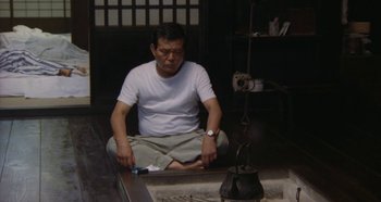 Movie still from “Rhapsody in August” (1991), directed by Akira Kurosawa – A man sitting on the ground in front of an open fire; Medium shot, High angle