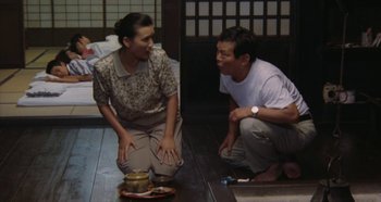 Movie still from “Rhapsody in August” (1991), directed by Akira Kurosawa – A man and a woman sitting next to each other on the floor; Medium shot, High angle