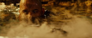 Movie still from “Riddick” (2013), directed by David Twohy – A man in a body of water looking at the camera; Extreme Close Up shot, High angle